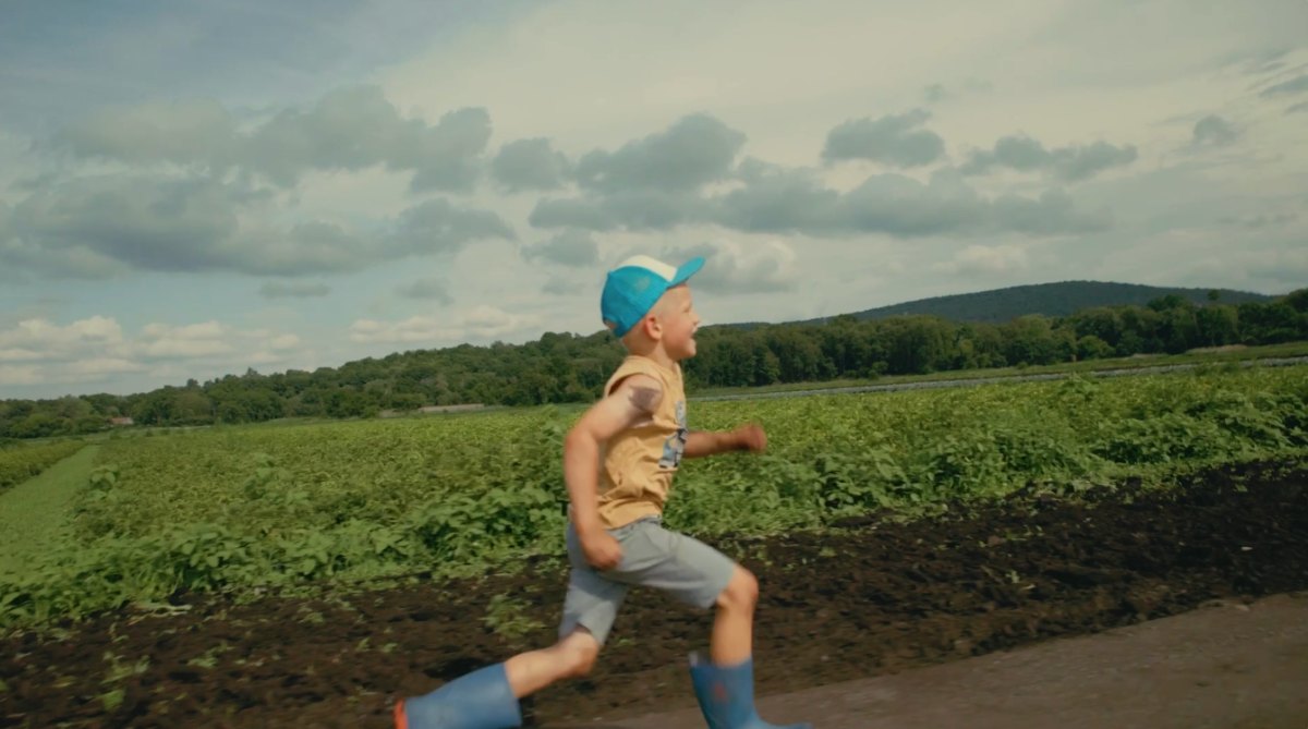 Boy running past a field, Farm to People